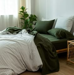 a bed with green sheets and pillows in a room next to a plant on the floor