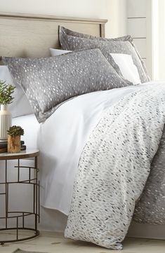 a bed with white and grey comforters in a bedroom next to a night stand