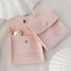 two pink pouches with pearls on them sitting next to a seashell and shell