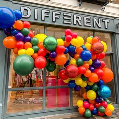 a bunch of balloons that are in front of a store window with the words different on it