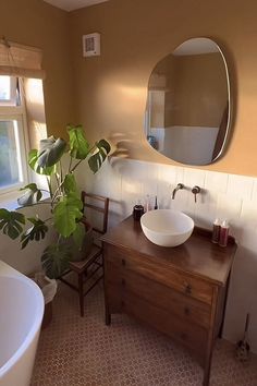 a bathroom with a sink, mirror and bathtub next to a large potted plant