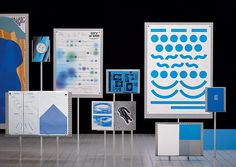 an assortment of blue and white art on display in front of a black wall with posters