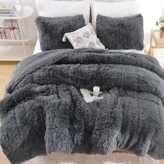 the comforter is made up with fluffy grey blankets and pillows on top of it