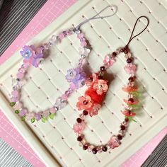 three bracelets with flowers and beads are on a white tray next to a pink background