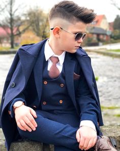 a young man sitting on top of a rock wearing a suit and tie with sunglasses