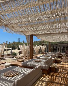 an outdoor lounge area with lots of white sheets on the ceiling and wooden flooring