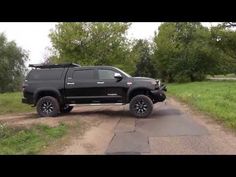 a black truck parked on the side of a dirt road next to grass and trees