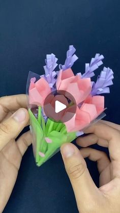 two hands are holding origami flowers with purple and pink petals