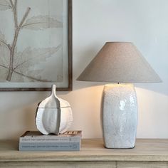 a white vase sitting on top of a wooden table next to a book and lamp