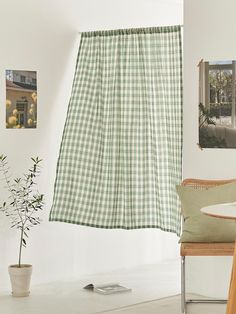 a green and white checkered curtain hanging in front of a window with a potted plant next to it