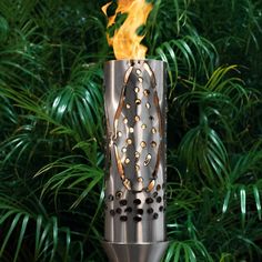 a metal fire pit with flames coming out of it's sides in front of some plants