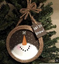 a snowman ornament hanging from a tree with a sign that says let it snow