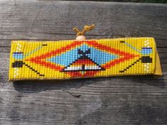 a yellow beaded wristband with an orange and blue design on the front, sitting on a wooden surface