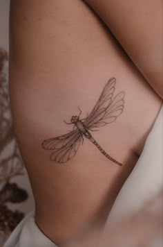 a woman's stomach with a tattoo of a dragonfly on her left side