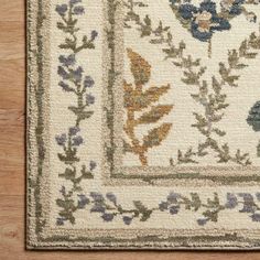 an area rug with blue flowers and green leaves on the border, in front of a wooden