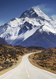 an empty road in front of a snow covered mountain