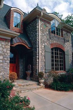 a stone house with arched windows and shutters on the front door is surrounded by greenery