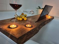 a wooden tray with candles and some fruit on it next to a glass of wine