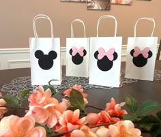 four bags with minnie mouse ears on them sitting on a table next to pink flowers