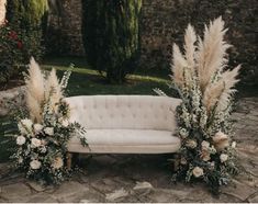 a white couch sitting on top of a stone floor next to tall grass and flowers