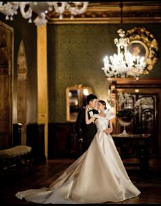 a bride and groom posing for a photo in an ornate room with chandeliers