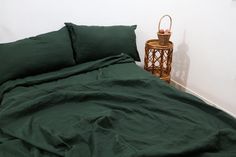 a bed with green sheets and pillows next to a small basket on the side table