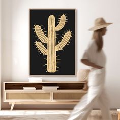 a woman in white is walking past a large cactus print on the wall above a tv