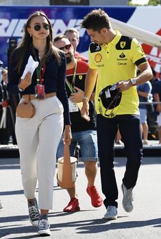 a woman in white pants walking next to a man wearing a yellow shirt and black jacket