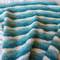 a blue and white crocheted blanket laying on top of a bed