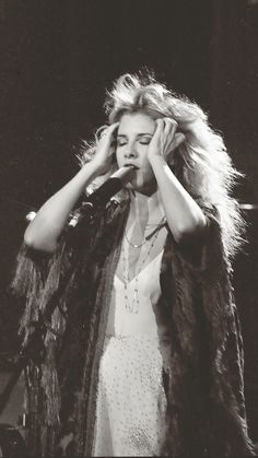 a black and white photo of a woman holding her hands up to her face as she sings