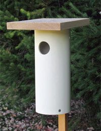 a white bird house sitting on top of a wooden post in front of some trees