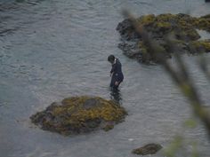 a man standing in the middle of a body of water next to green moss covered rocks