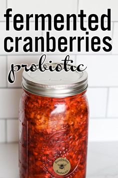 a glass jar filled with cranberries on top of a counter next to a white tile wall