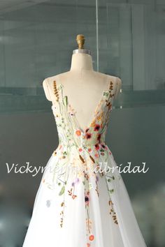 a white dress with colorful flowers on the front and back, is displayed in a glass case