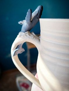 a bird figurine sitting on top of a white coffee cup in front of a blue wall