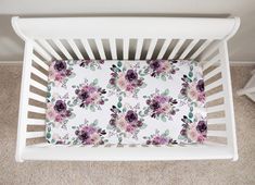 a white crib with flowers and leaves on the bottom half, in front of a carpeted wall