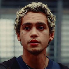 a close up of a person wearing a black shirt and earring with tattoos on his face