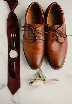 a pair of brown shoes next to a tie and watch