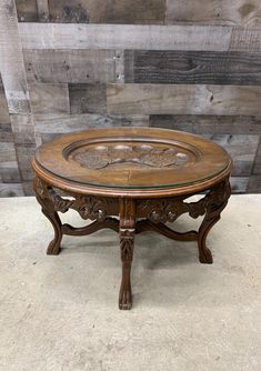 an ornately carved wooden table with glass top on concrete floor in front of wood paneled wall