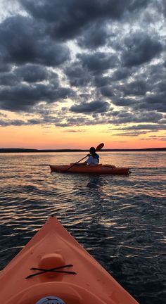 a person in a kayak paddling on the water at sunset with dark clouds