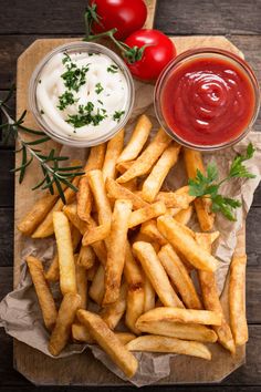 french fries with ketchup and tomatoes on a cutting board next to dipping sauce