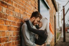 a man and woman hugging against a brick wall