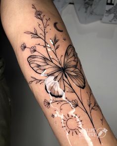 a black and white photo of a butterfly on the arm, with flowers in it