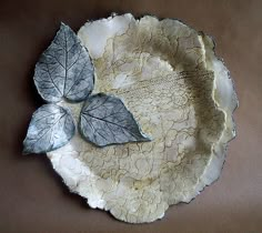 two leaf shaped plates sitting on top of a brown cloth covered tablecloth with white lace