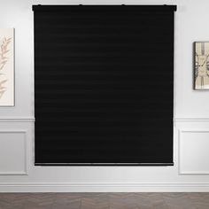 a black roller shade hangs on the wall in an empty room with white walls and wood flooring