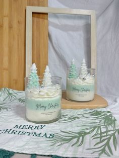 two jars with frosted christmas trees in them sitting on a table next to a wooden frame