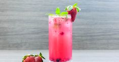 two strawberries sit on the table next to a tall glass filled with pink liquid