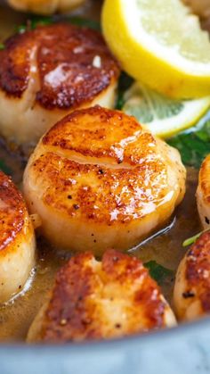 seared scallops cooking in a pan with lemon wedges