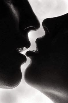 two people kissing each other with their noses close to one another in front of a cloudy sky