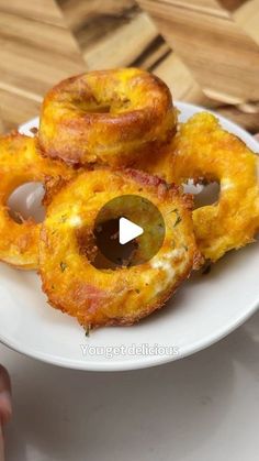 a white plate topped with onion rings on top of a wooden table next to a person's hand